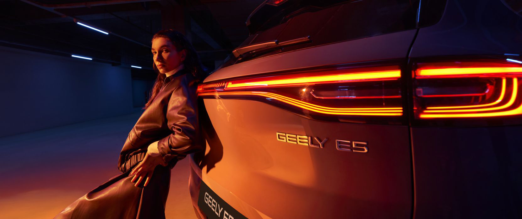 Kobieta opierająca się nocą o samochód GEELY E5